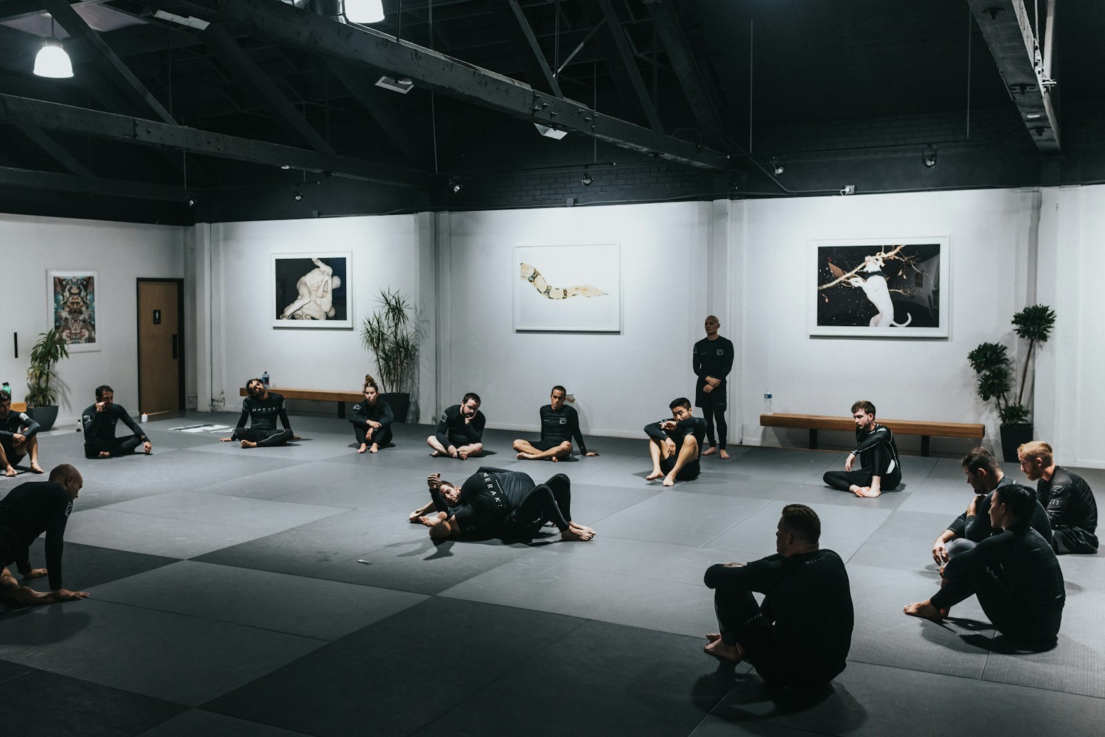 Students sitting along the wall of a matted gym, watching a class