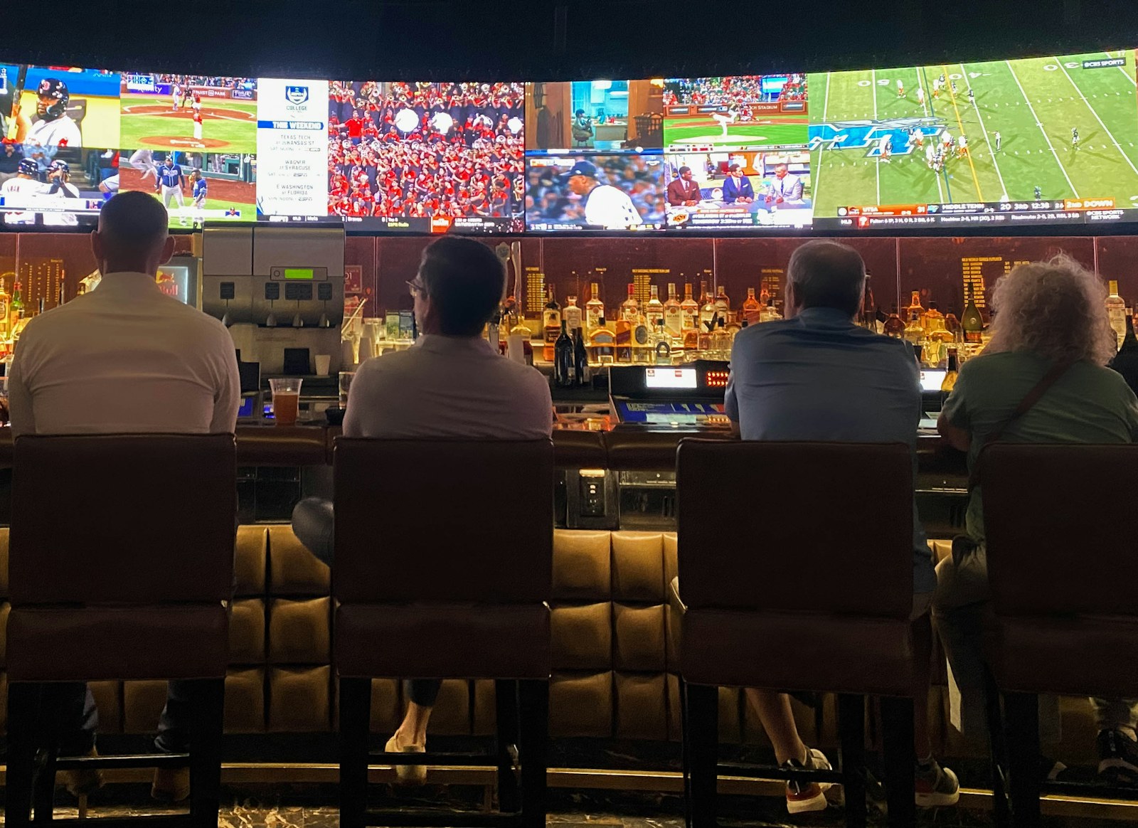 People sitting at a sports bar watching a row of screens, where you'd watch UFC in Honolulu with company.