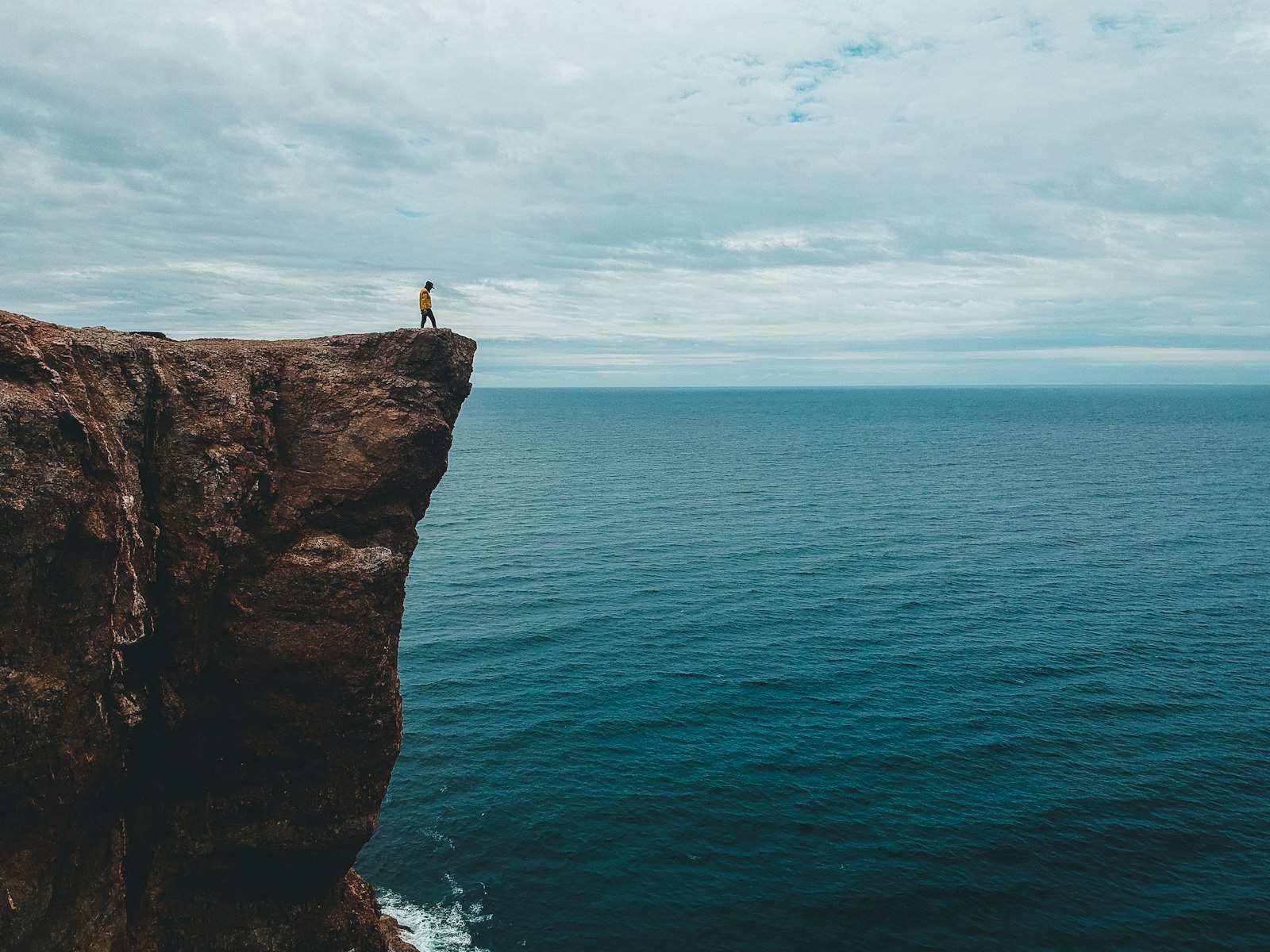 A lone figure standing at the edge of a high cliff, facing an empty ocean horizon.