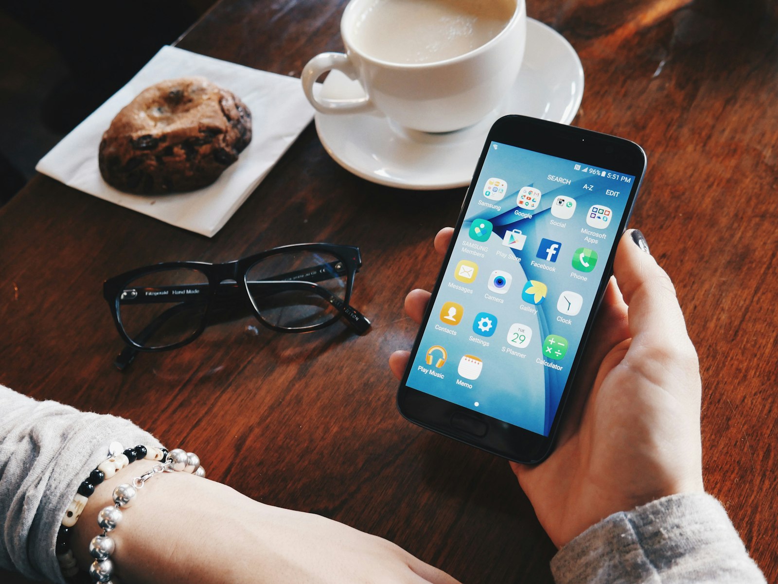 A phone held over a cafe table, its screen full of app icons, a coffee going cold beside it.