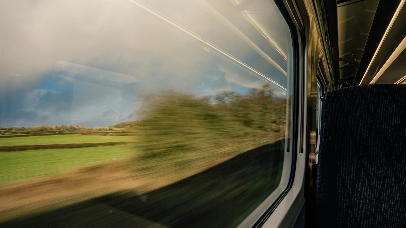 Green countryside passing outside the window of a passenger train.