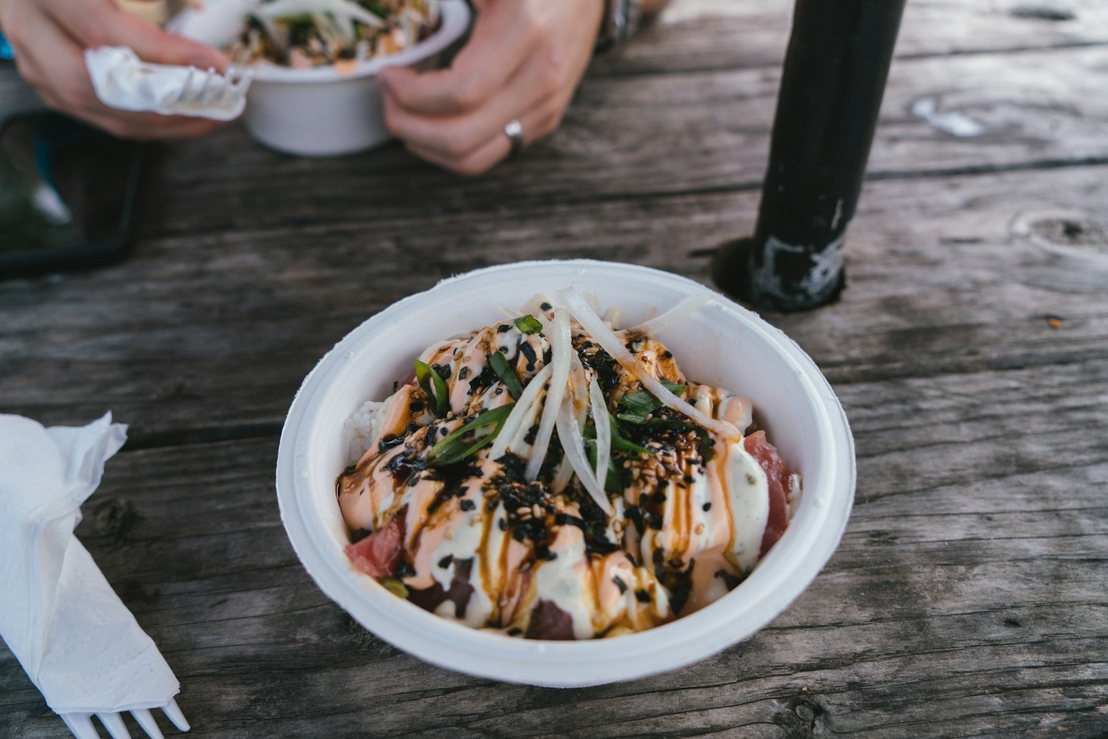 Poke bowl in a takeout container on a wooden picnic table