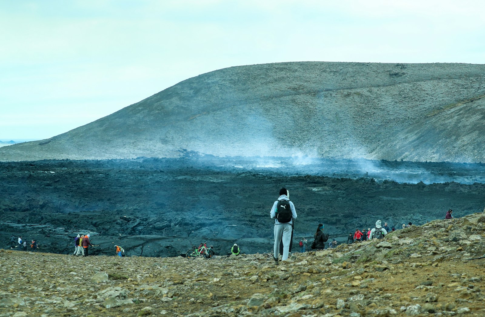 Two people walking together across a wide volcanic plain toward a distant crater.