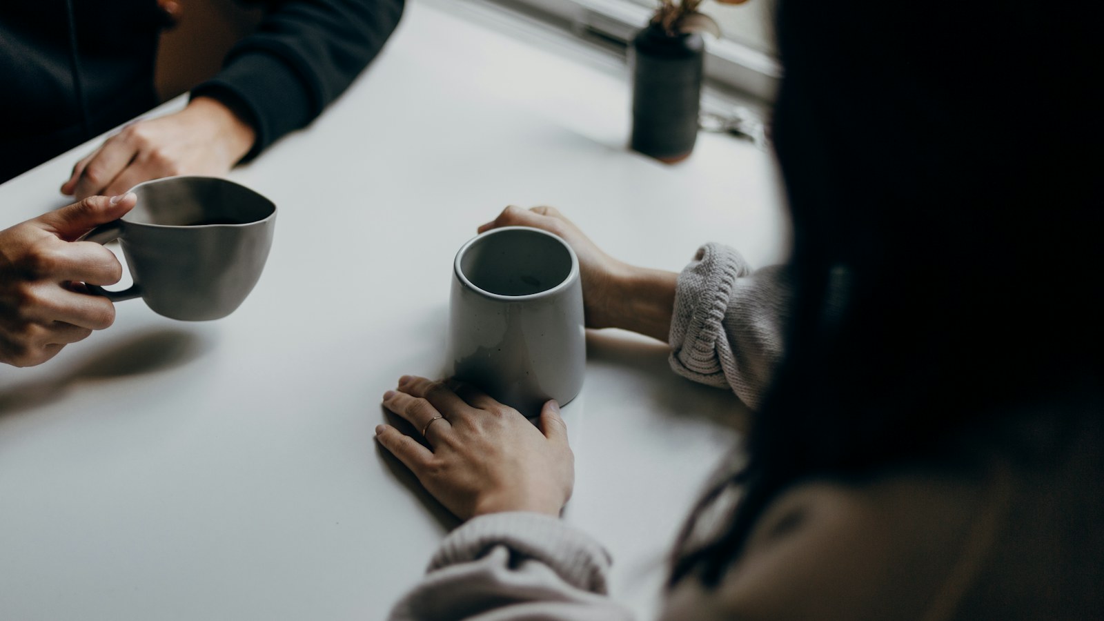 Two people holding coffee mugs across a white table.