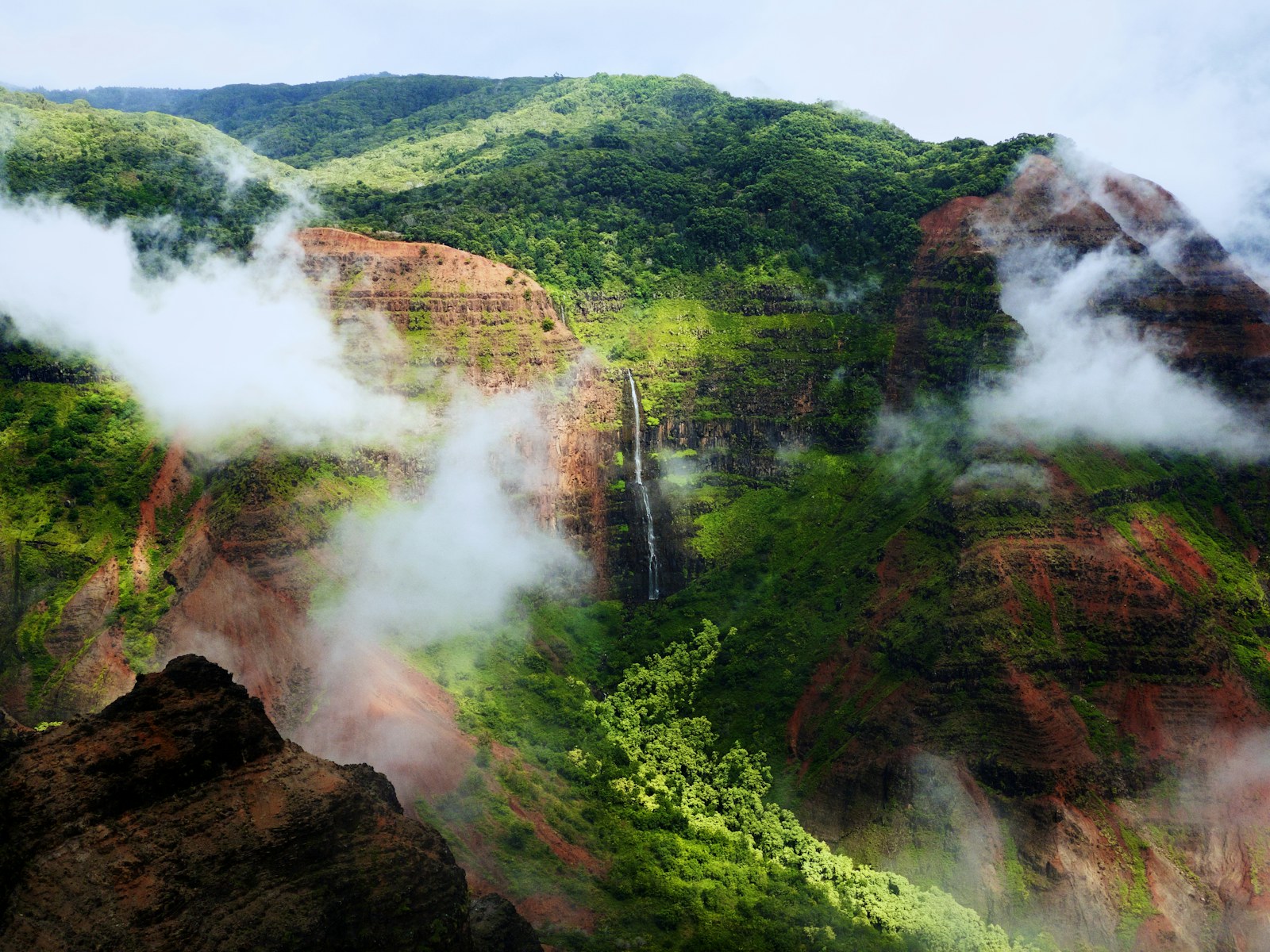 Waimea Canyon on Kauai with a waterfall and low clouds, one of the Kauai hikes for beginners.
