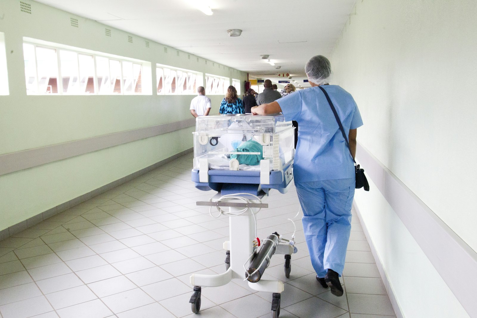 A nurse in scrubs pushing equipment down a hospital corridor