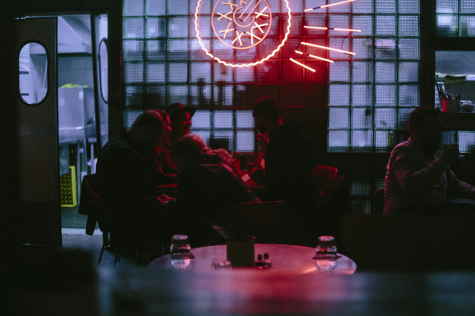 A group huddled around a table in a dim bar lit by a neon sign