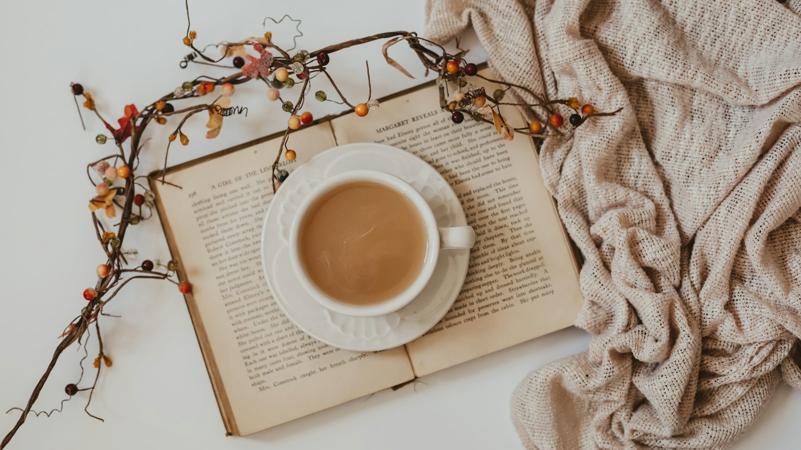 An open book and a cup of coffee beside a knitted blanket.