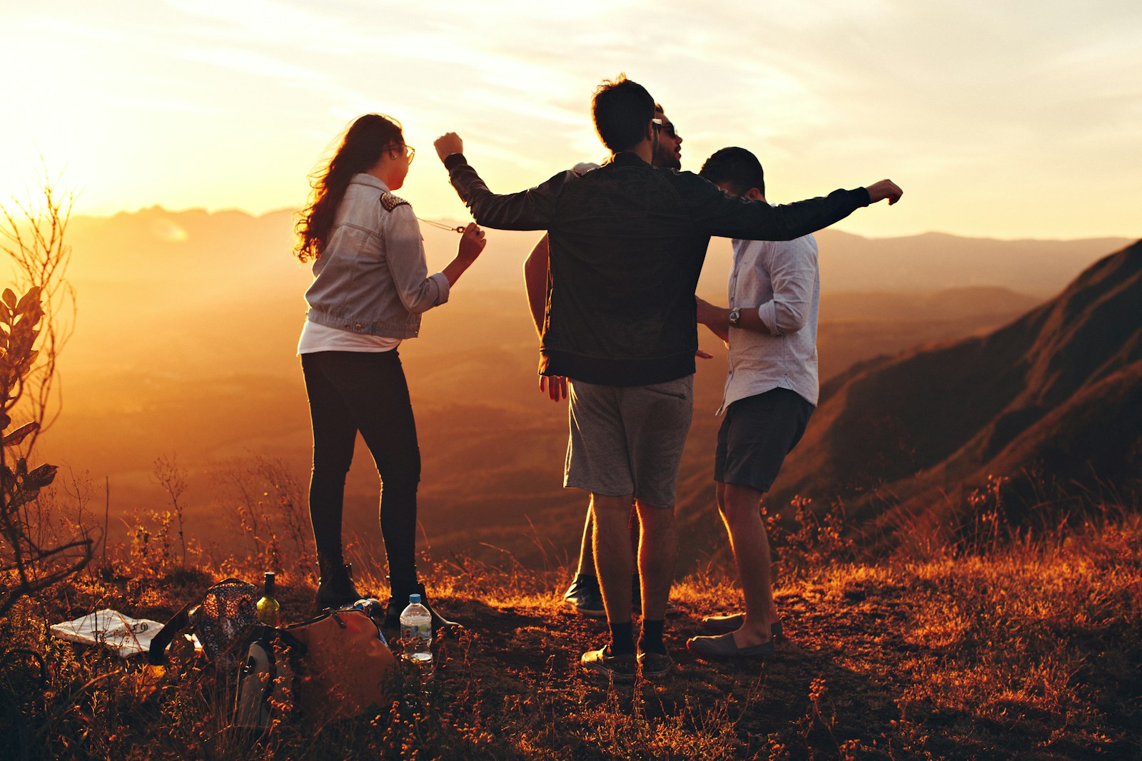 Four friends standing on a ridge at sunset, arms up, the kind of real plan YKnot is for.