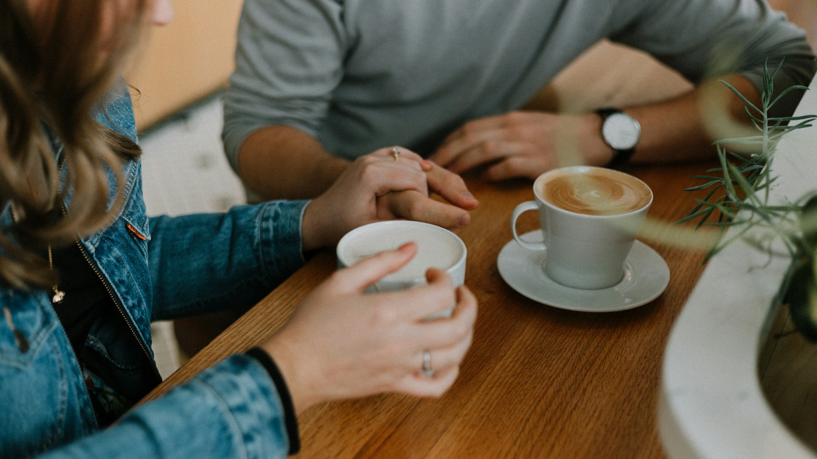 People holding coffee cups while talking across a wooden table.
