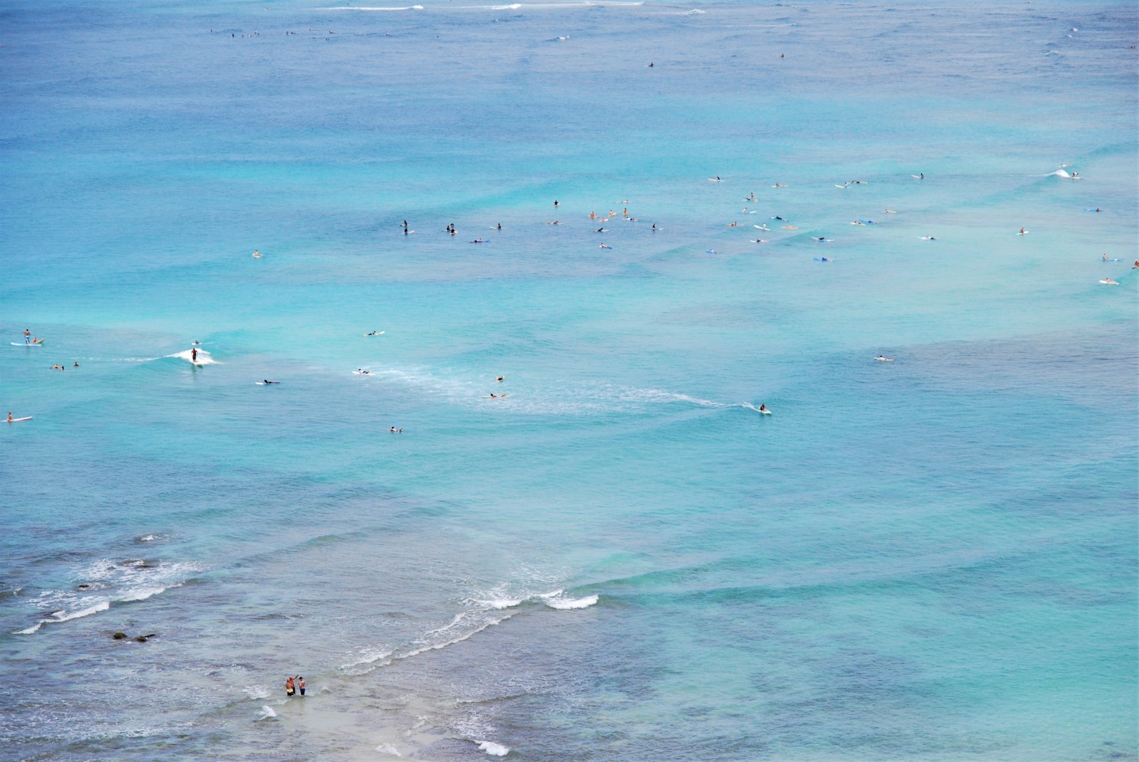 Aerial view of surfers waiting for waves in the turquoise water off Waikiki, one of the best beginner surf spots on Oahu.