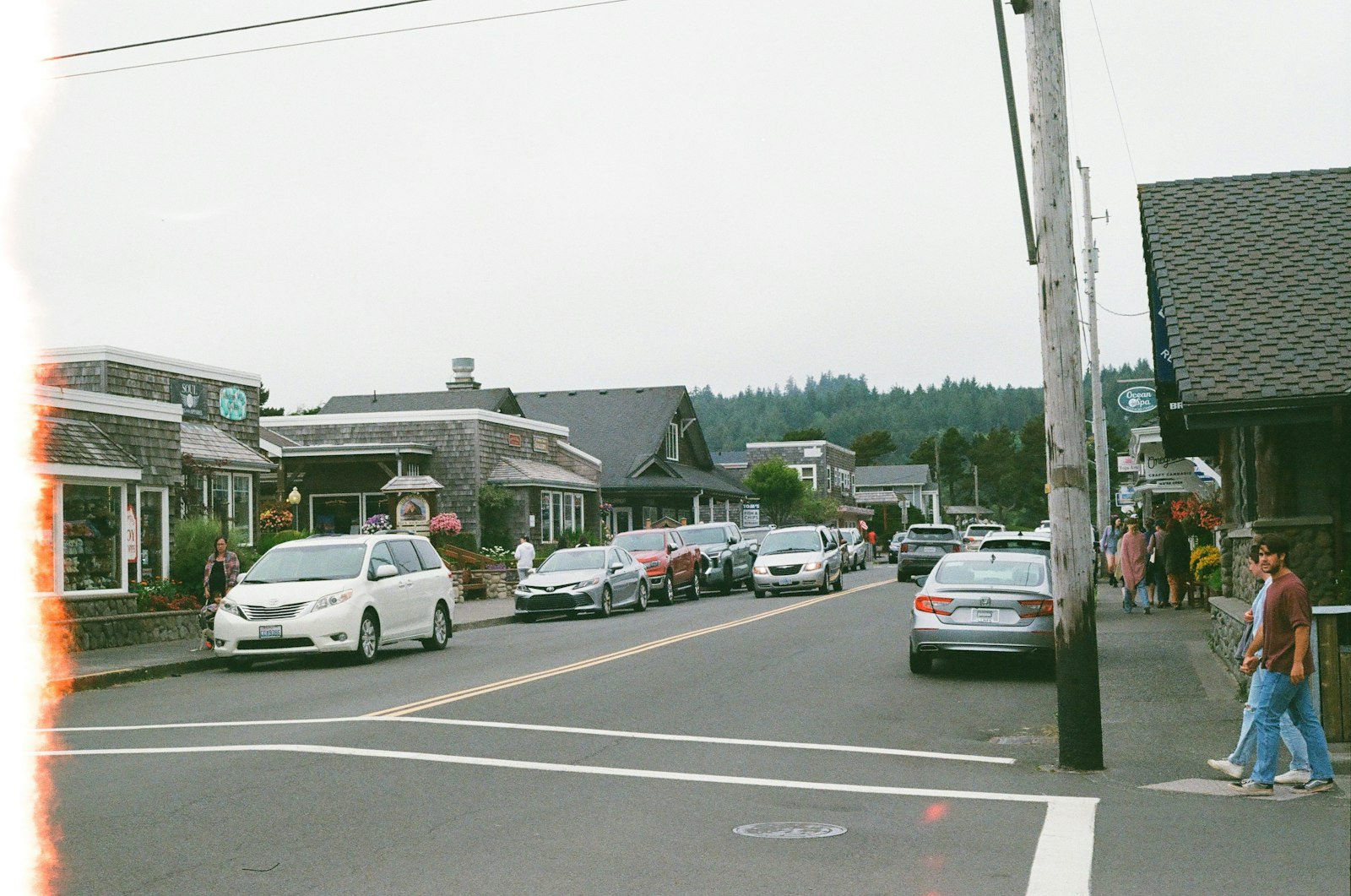 A small town's one main street, cars parked nose-in outside low wooden storefronts and a few people crossing.