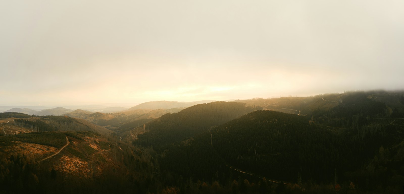 A wide valley of low ridges under haze at the end of the day, seen from higher up the slope.