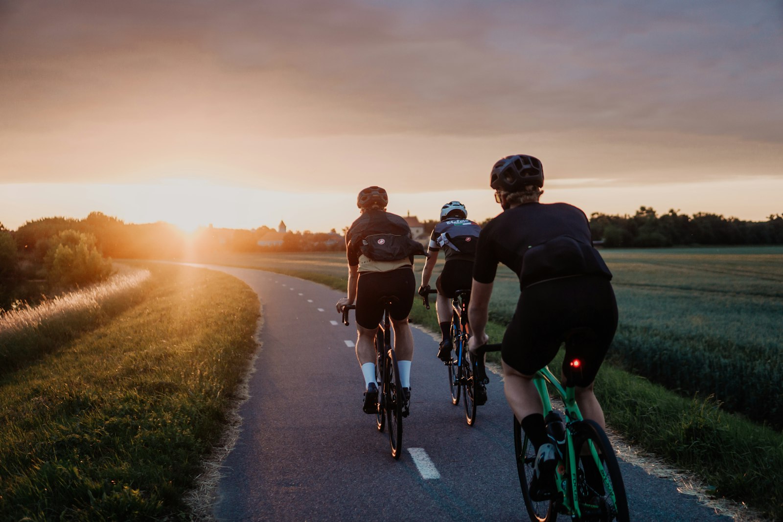 A group of cyclists riding into low sun on an empty road