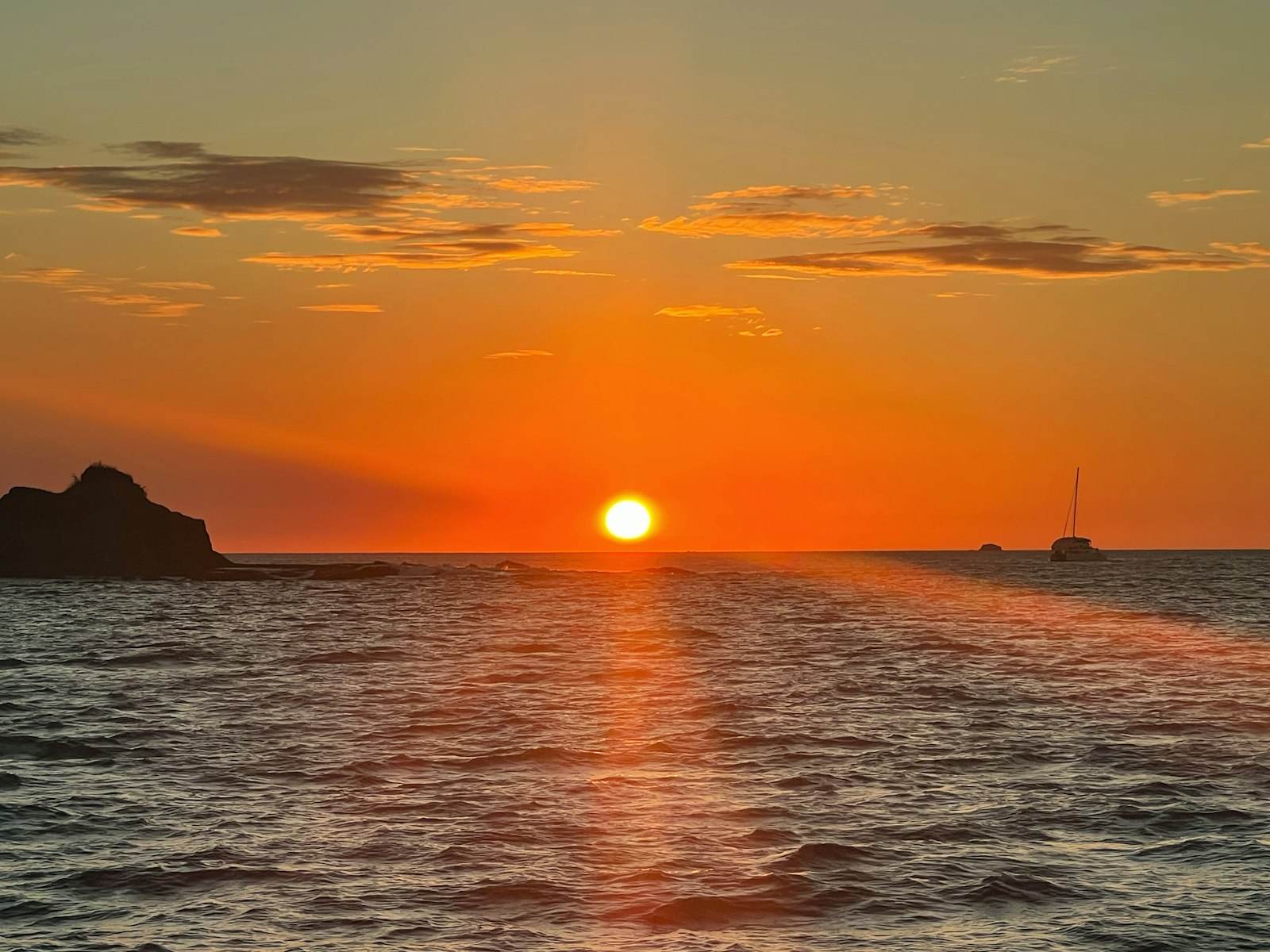 The sun on the horizon at dusk with a catamaran silhouetted on the water to the right