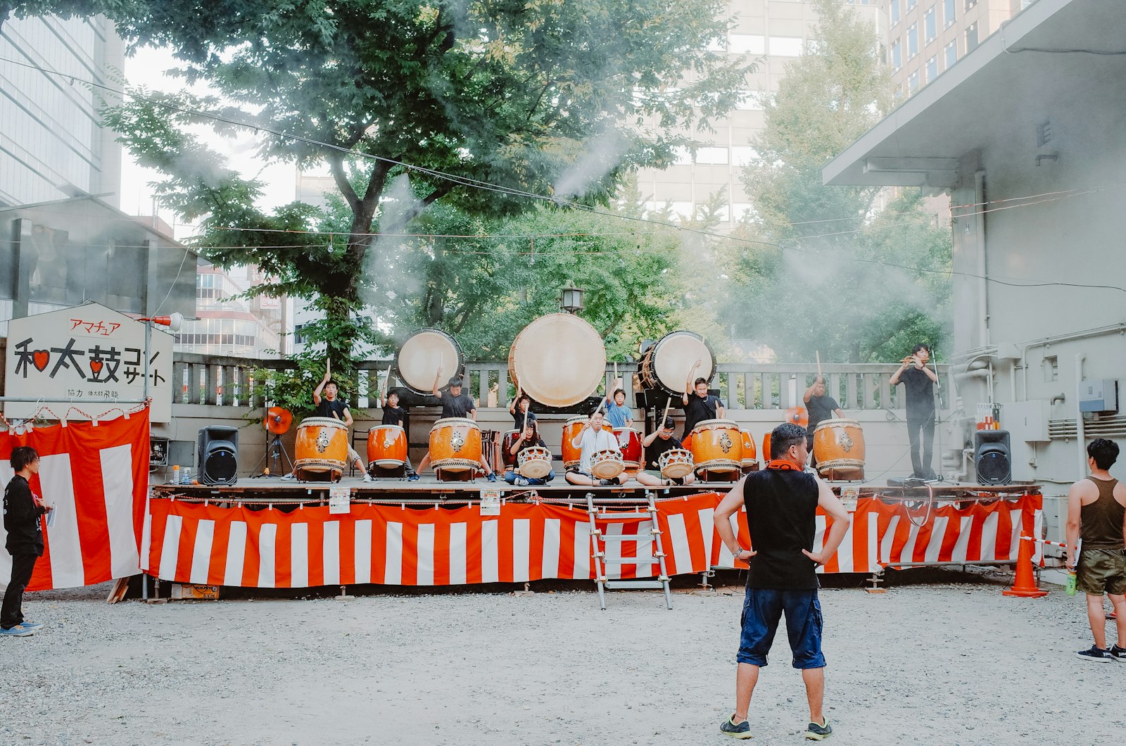 Taiko drummers playing at an outdoor summer festival, red and white bunting strung behind them.
