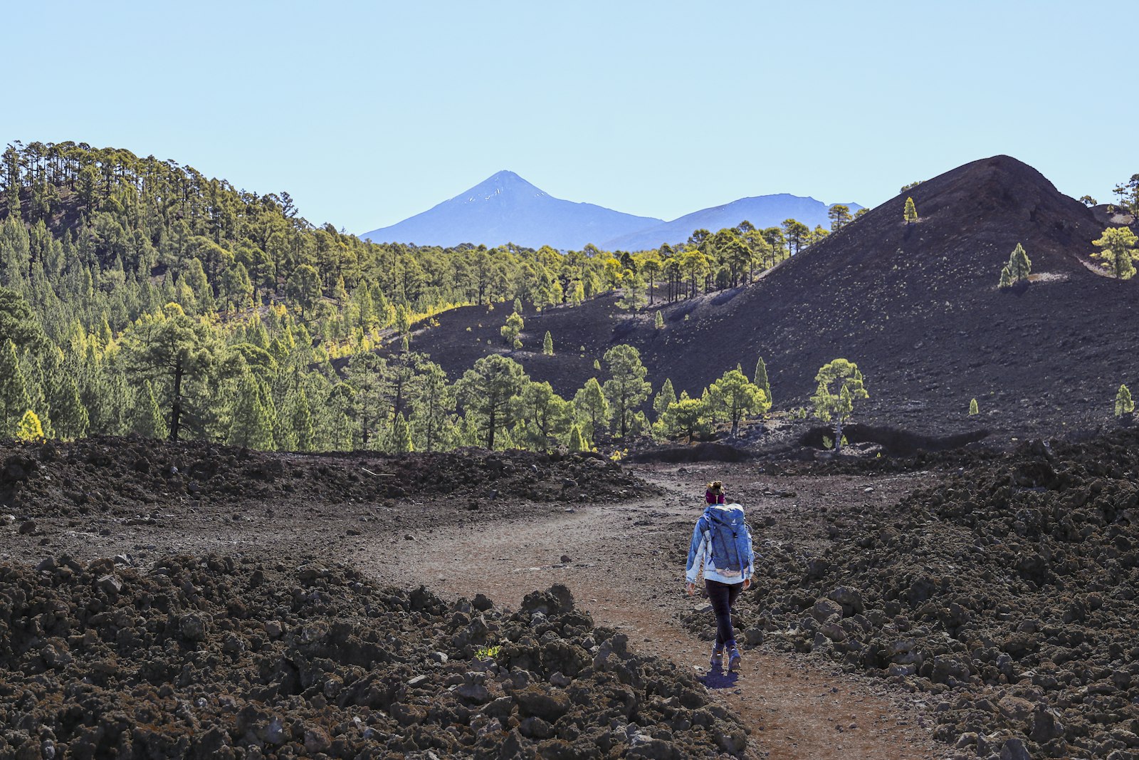 A hiker walking a path across an old lava flow toward a volcano
