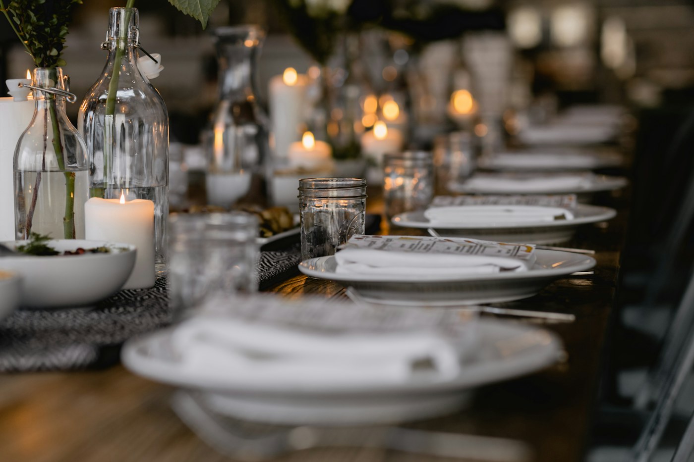 A dining table set with plates, candles, and glass bottles