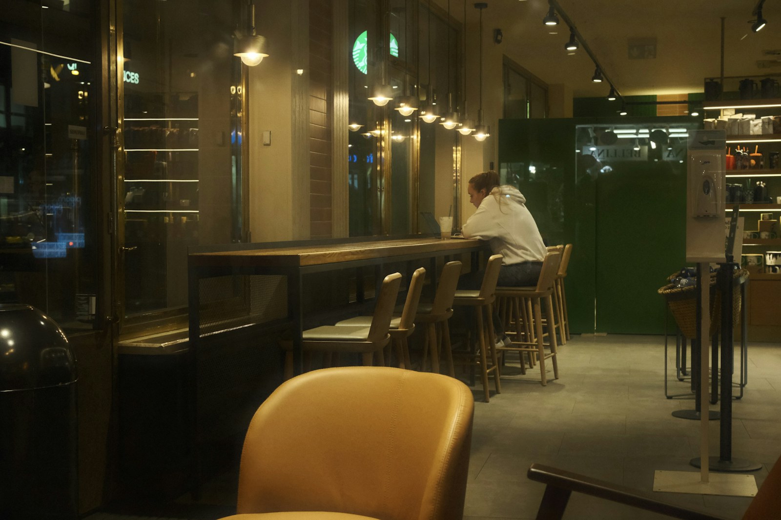 A single person sitting alone at a cafe counter with empty stools beside them.