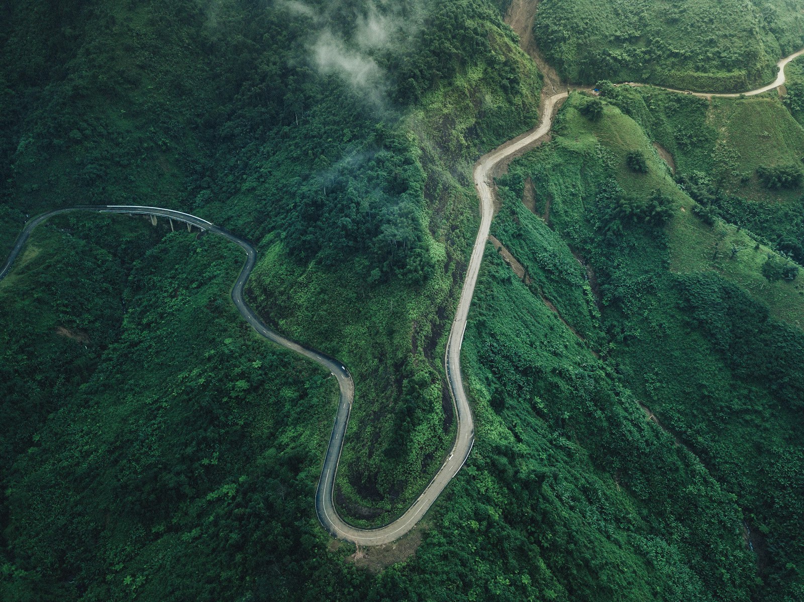 A road winding through steep green mountains, seen from above