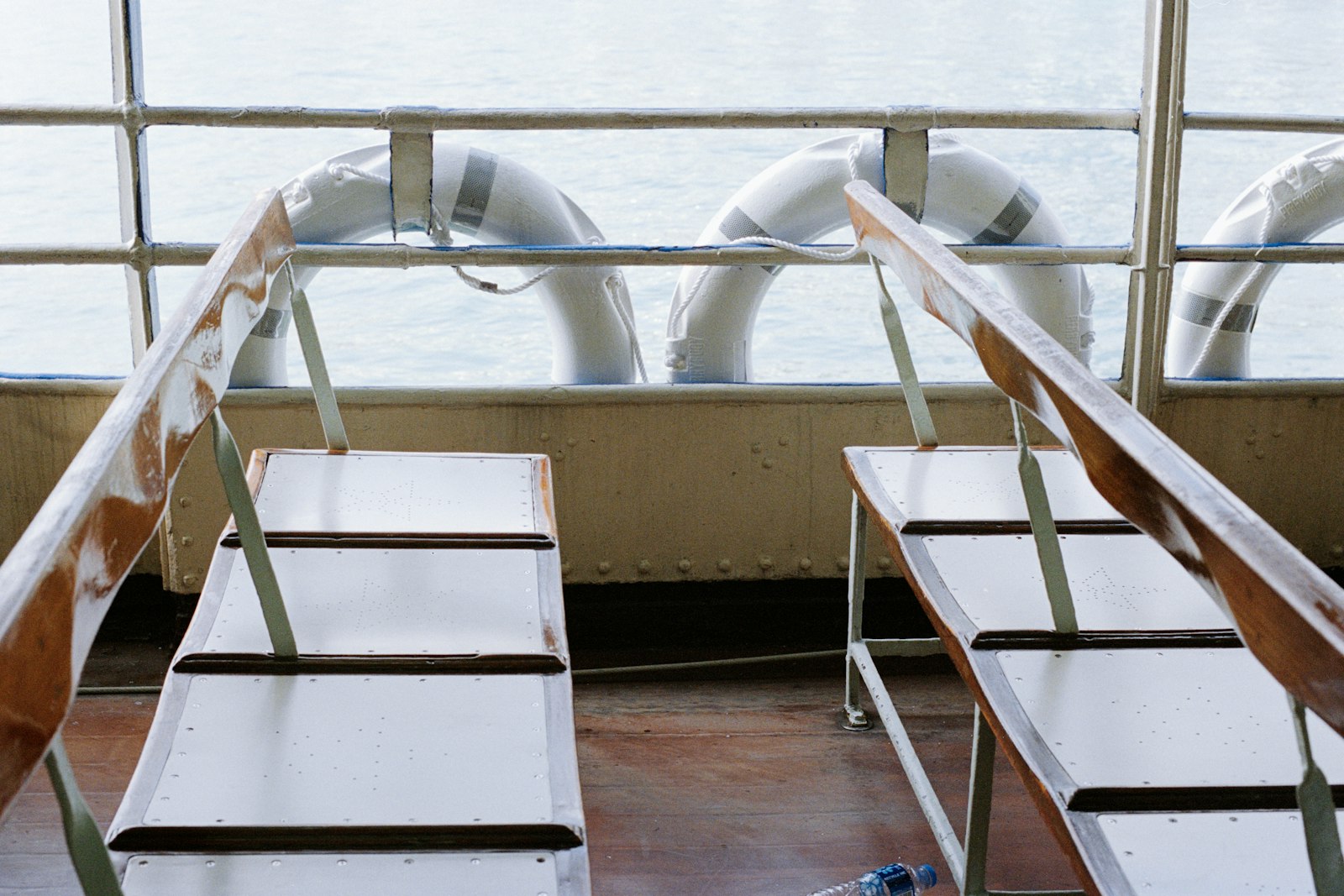 Empty white benches on a boat deck, life rings hanging on the rail and flat water beyond.