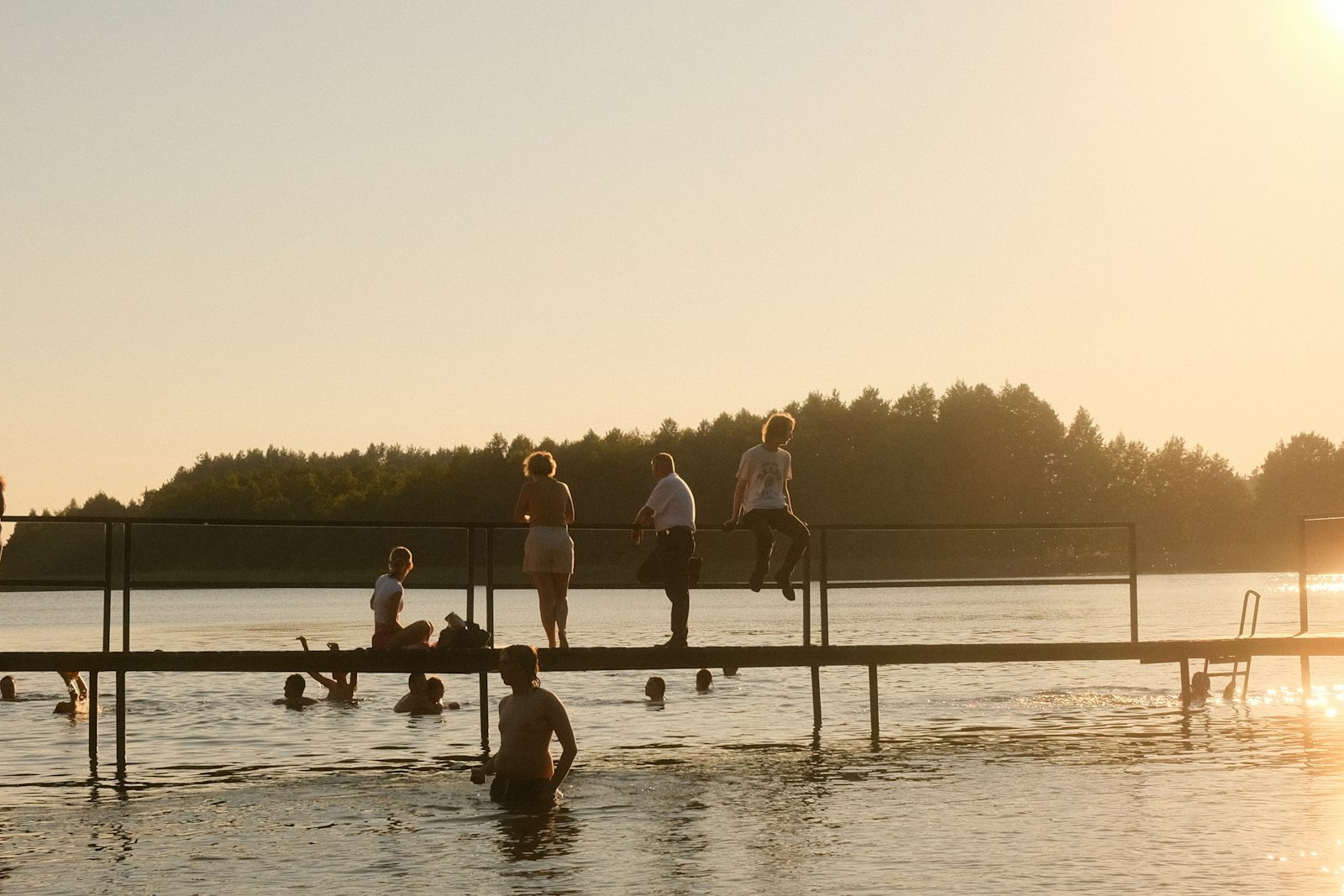People gathered on a pier at sunset, some of them in the water