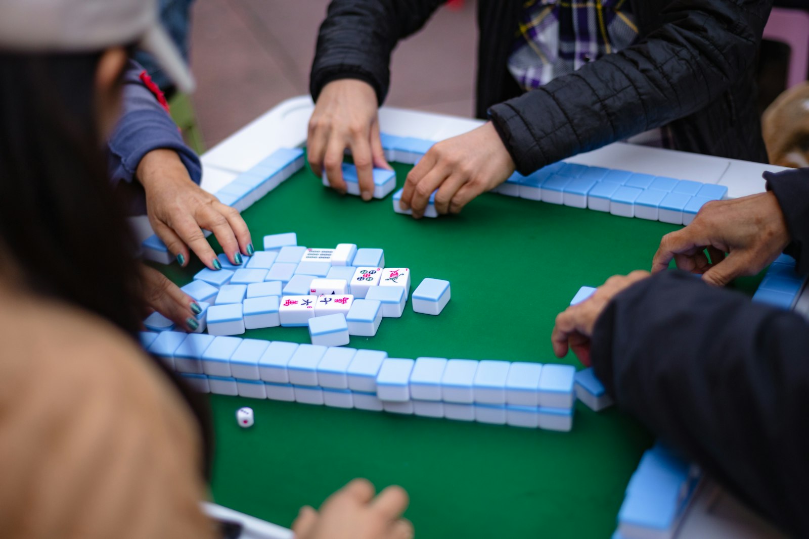Four players' hands at a green mahjong table, tiles built into walls in front of each of them mid-game.
