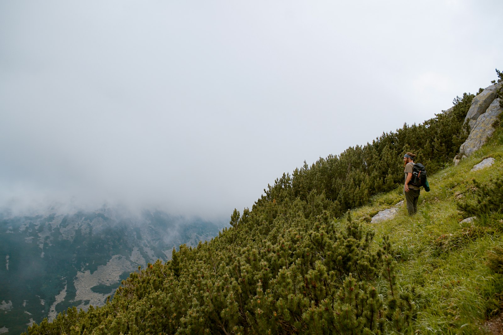 A hiker on a green ridge with cloud rolling across it