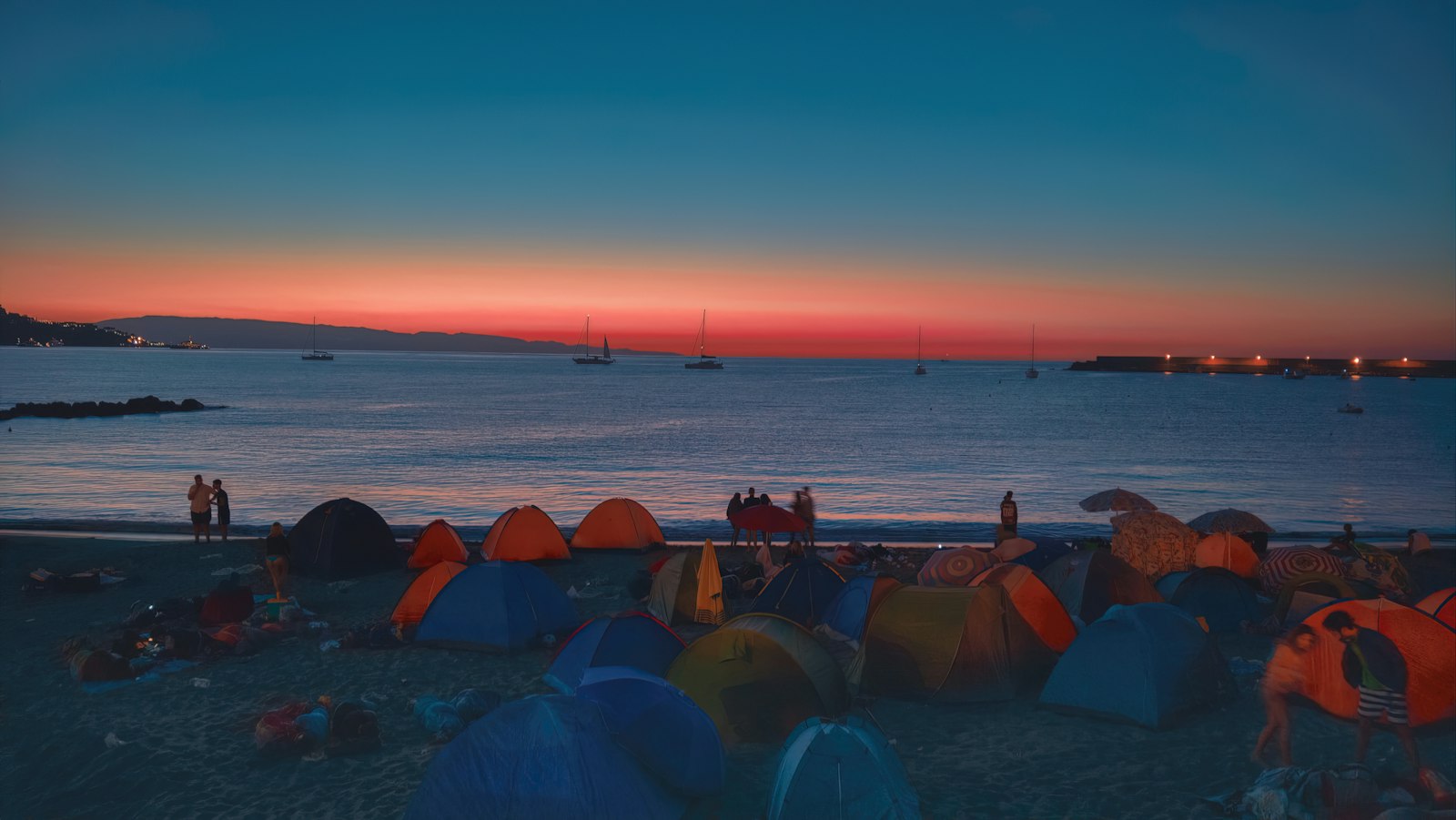 Rows of tents pitched along a beach at sunset, people moving between them.