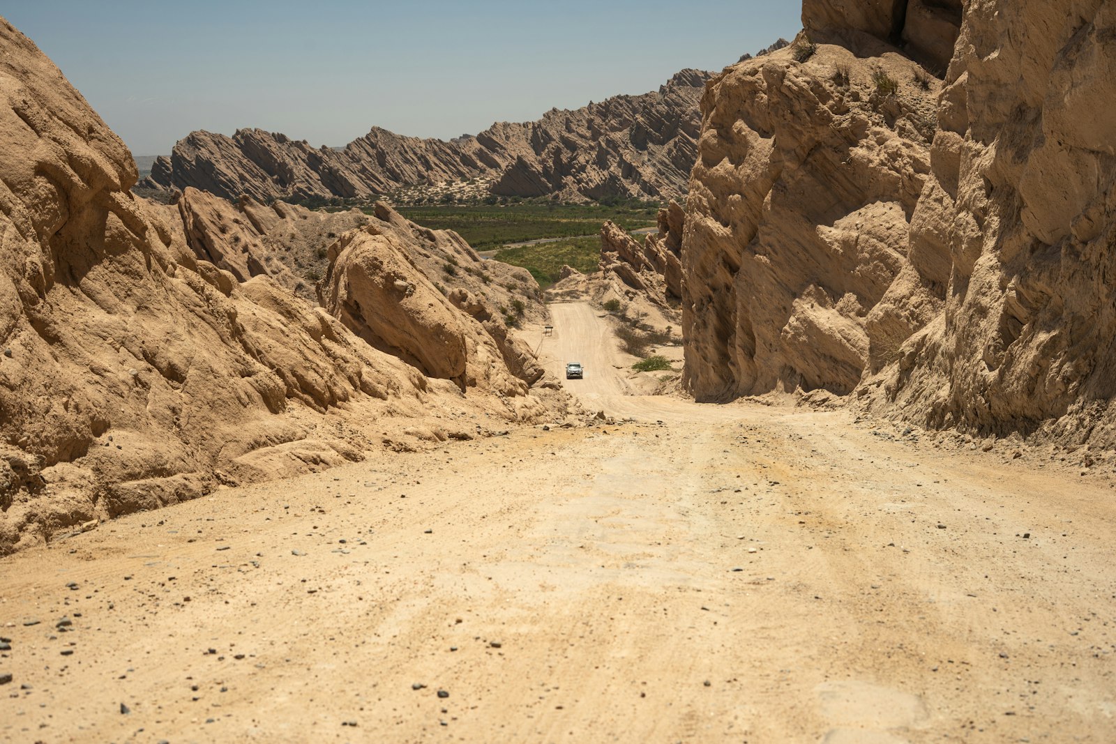A dirt track running between tall red and tan canyon walls under an open sky.