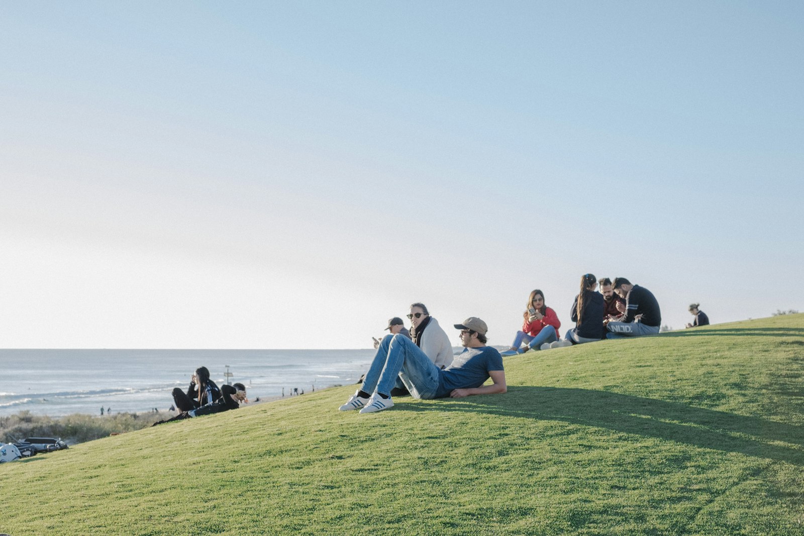 People sitting on the grass above a beach at the end of the day