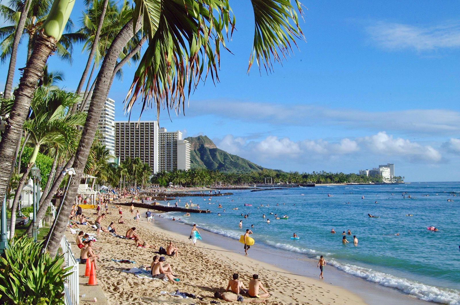 Waikiki Beach lined with palm trees, with swimmers in turquoise water and Diamond Head in the background.