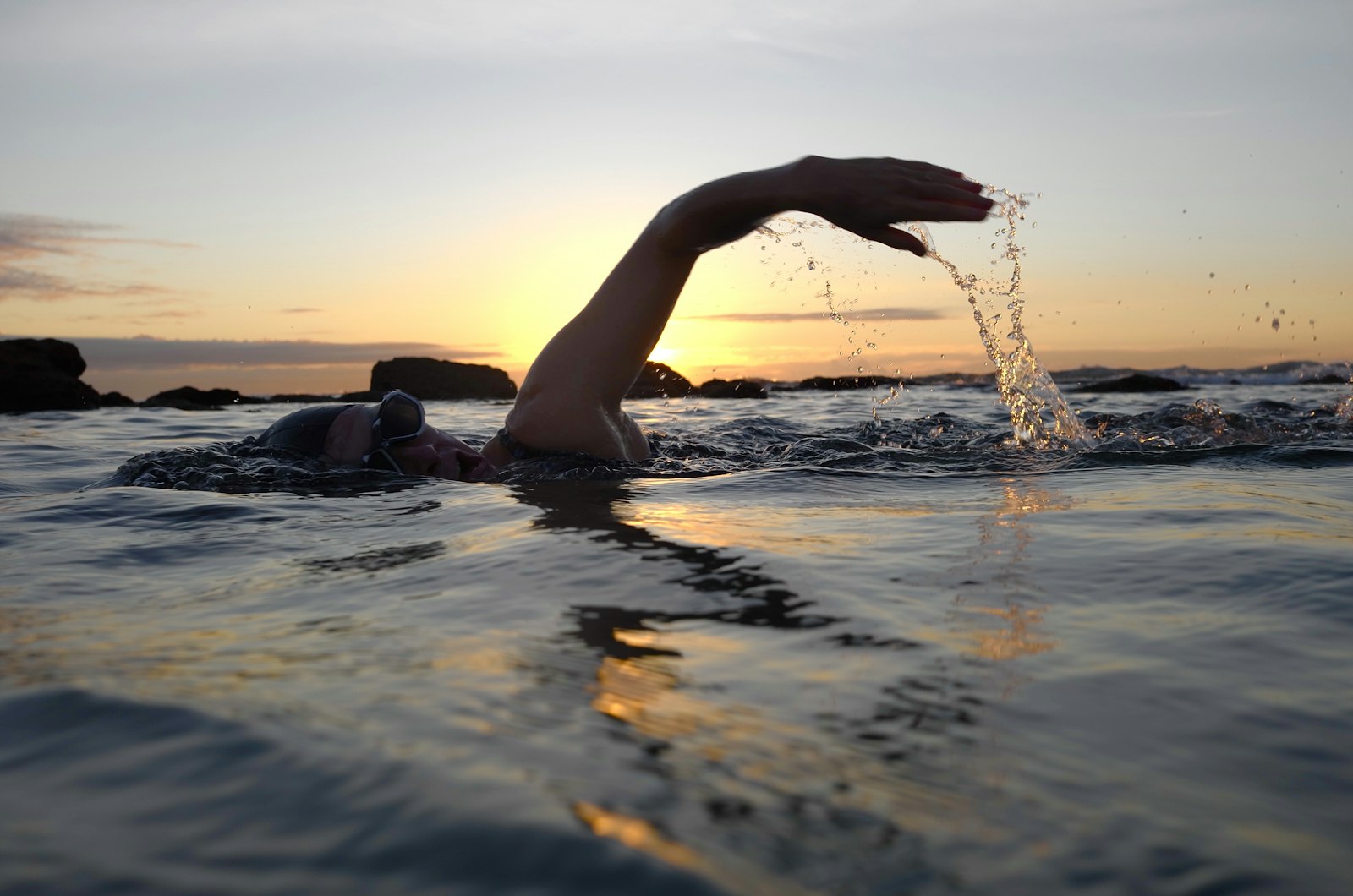 A swimmer mid-stroke in open water at sunrise