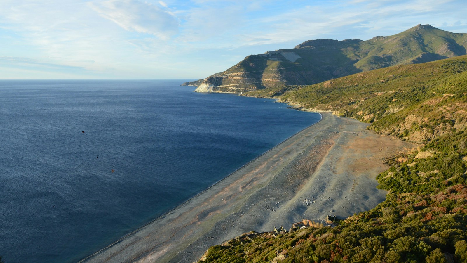 Dry, steep mountains dropping straight into deep blue water along an exposed coast.