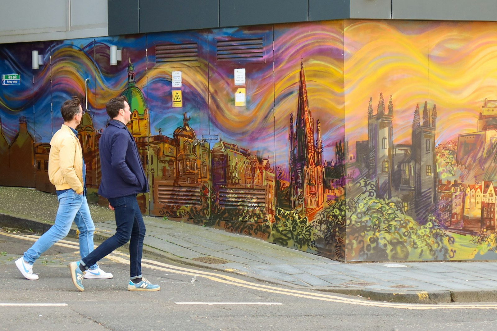 Two people walking past a painted mural on a city street