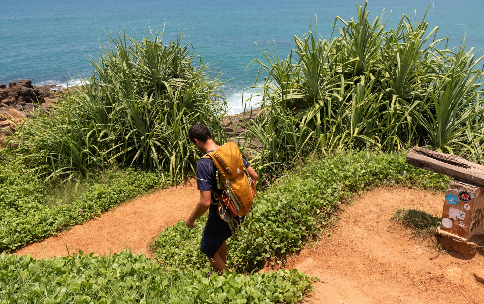 A person with a backpack walking a red-dirt coastal path alone