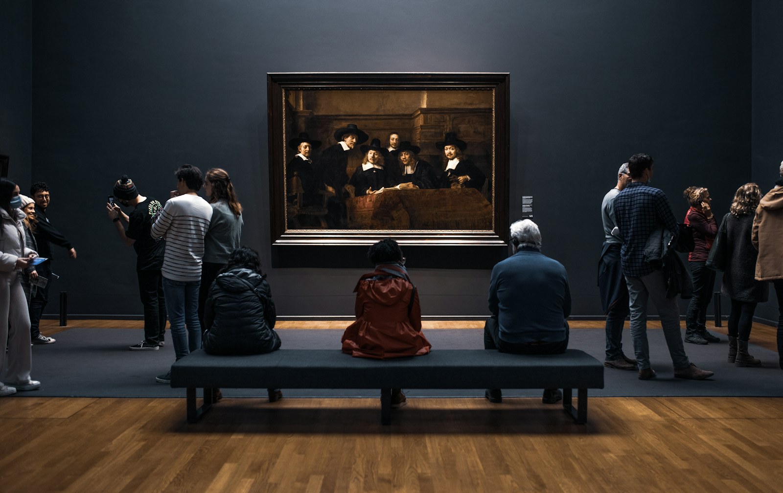 A group of people gathered in front of a large painting in a museum gallery, like a First Friday Honolulu art night.